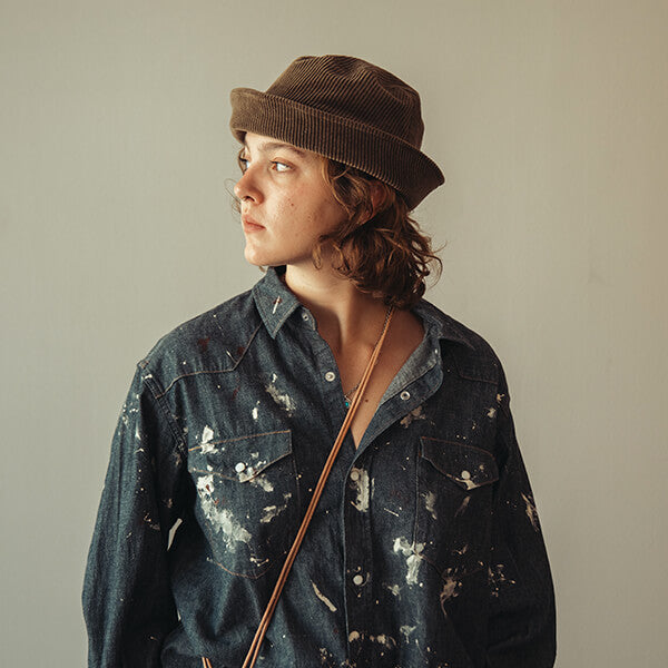 Model wearing a brown corduroy bucket hat, distressed indigo denim shirt